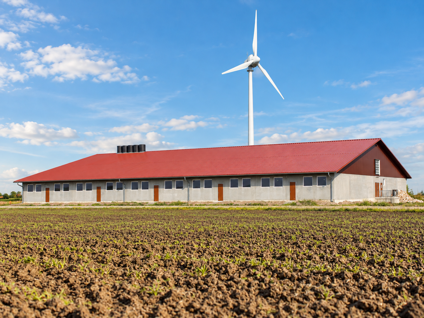 Modernisierte Aufnahme einer Stallanlage mit rotem Dach und Windenergieanlage